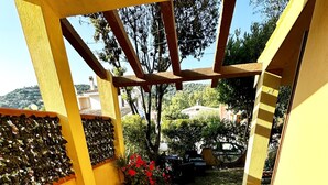 An outdoor patio with a table set for four, surrounded by white chairs, and a potted plant with red flowers.