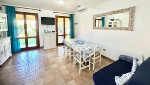 A room with a dining table, chairs, a sofa, a TV, a cabinet, and a large mirror.