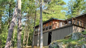 A cabin with a wooden deck and a covered porch, surrounded by trees and rocky terrain.