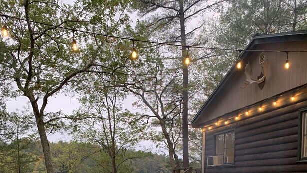 A rustic cabin with a fire pit, wooden deck, and string lights.