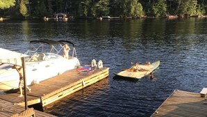 A wooden dock with a boat moored at the end, surrounded by calm water and a forested shoreline.