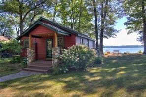 Une cabane rouge avec des fondations en pierre, une véranda et une vue sur un lac.