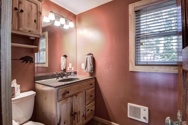 Un baño con tocador de madera, lavamanos, espejo y ventana con persianas.