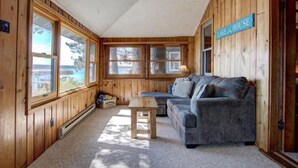 A cabin interior with a sofa, a small table, and large windows offering views of the outdoors. - Charming 2-bedroom Hayward Cabin on Lac Courte Oreilles (Hayward)