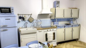 Cozinha compacta com geladeira, fogão, forno e micro-ondas. Há uma pia com torneira, uma mesa de jantar com cadeiras e uma janela acima do fogão.