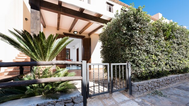 Un sendero de piedra que conduce a una entrada portonada, con una pérgola de madera en lo alto.