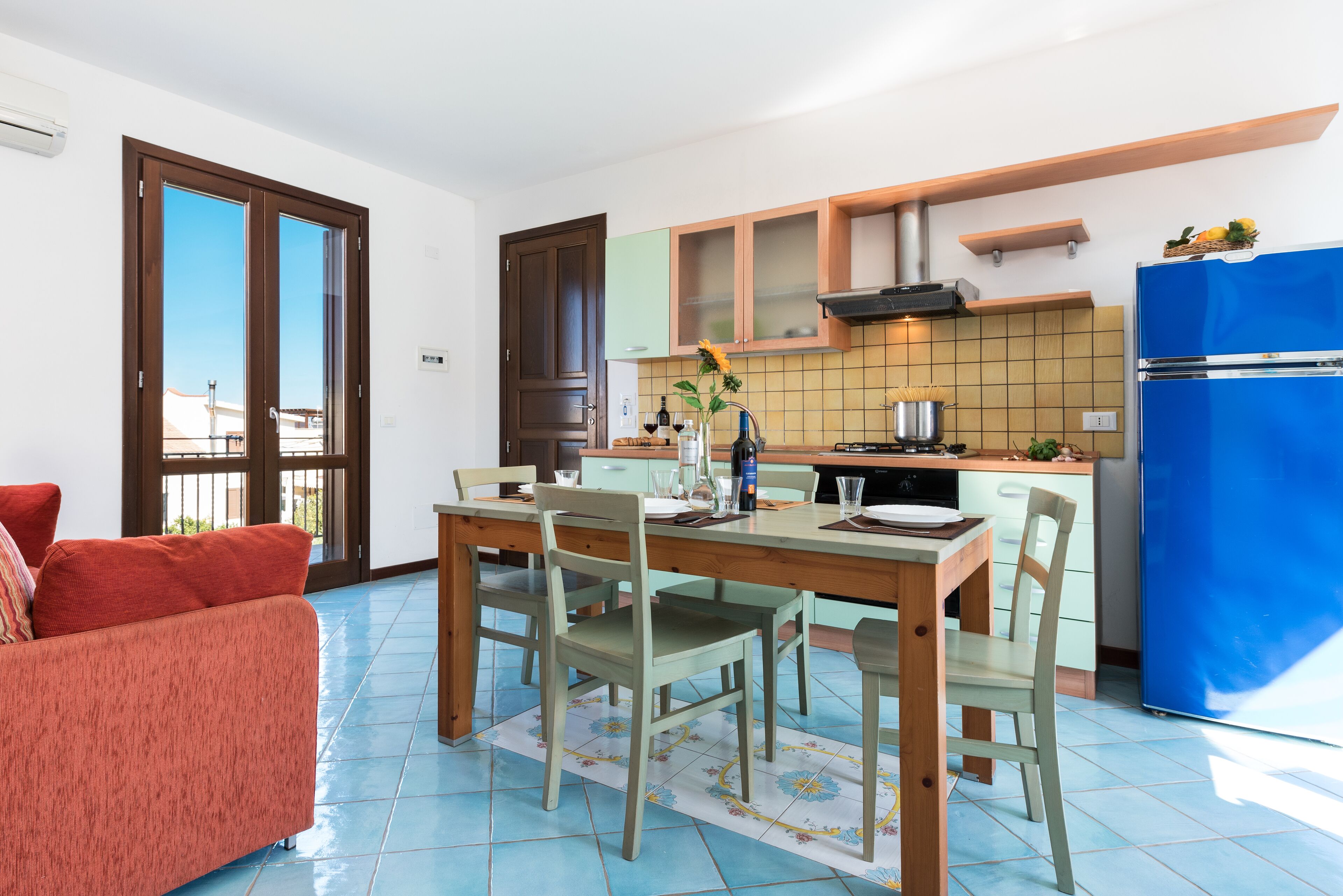 A modern kitchen with a dining table, chairs, and a blue refrigerator.