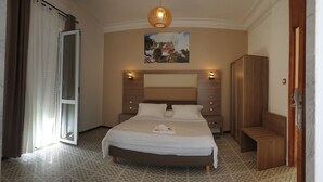 A bedroom with a large bed, a wooden wardrobe, a bench, and a painting on the wall. - Samir Hotel (Algiers)