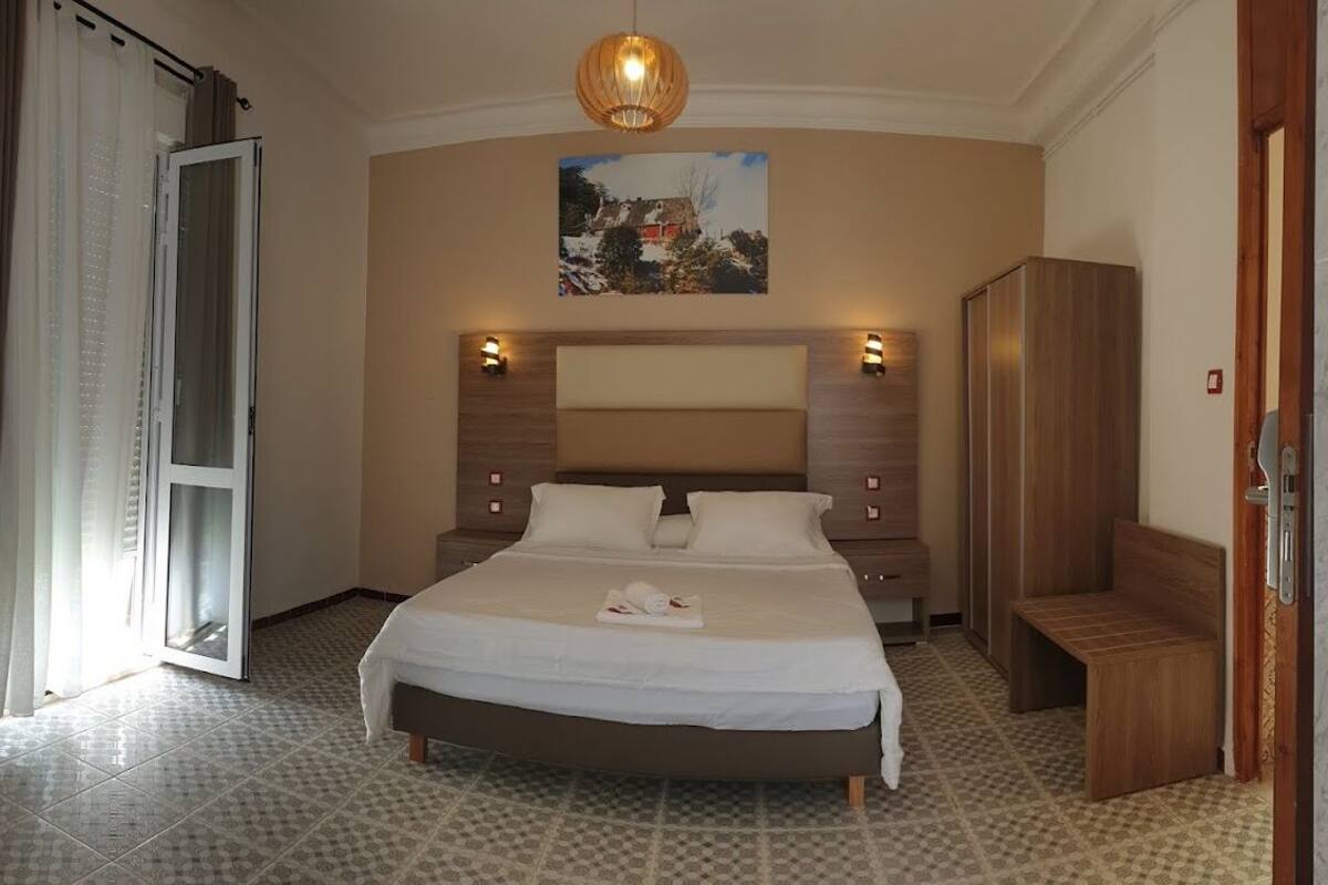 Un dormitorio con una cama grande, un armario de madera, un banco y un cuadro en la pared.