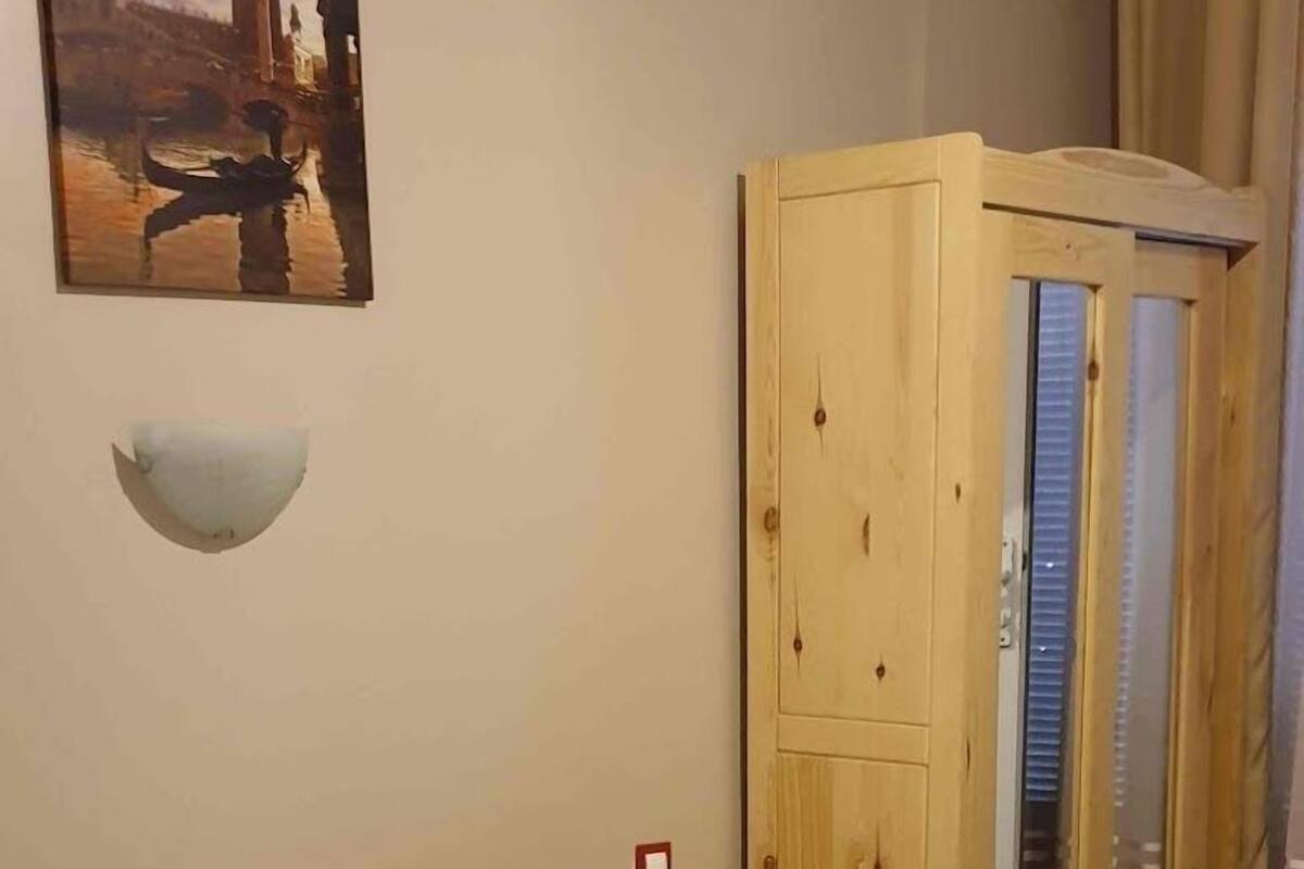 Una habitación de hotel con una cama, un armario de madera, un equipo de aire acondicionado y un cuadro de un paisaje urbano.