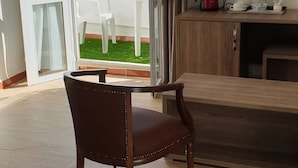 A living room with a dining table, a TV mounted on the wall, and a sliding glass door leading to an outdoor area with a white chair. - Samir Hotel (Algiers)