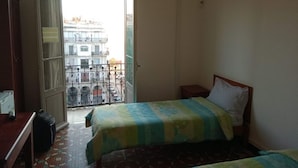 A hotel room with two beds, a desk, and a wardrobe. There is a balcony with a view of buildings. - Samir Hotel (Algiers)