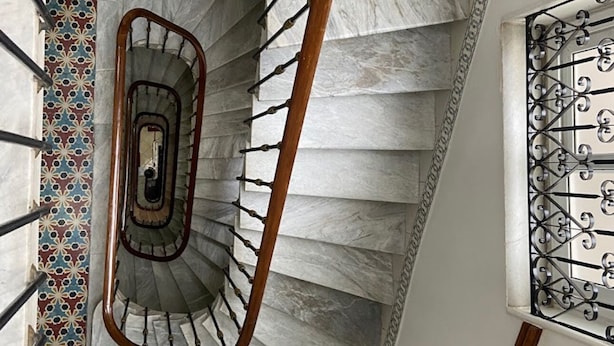 A spiral staircase with marble steps and a wooden handrail, surrounded by patterned tiles and a decorative metal gate. - Samir Hotel (Algiers)