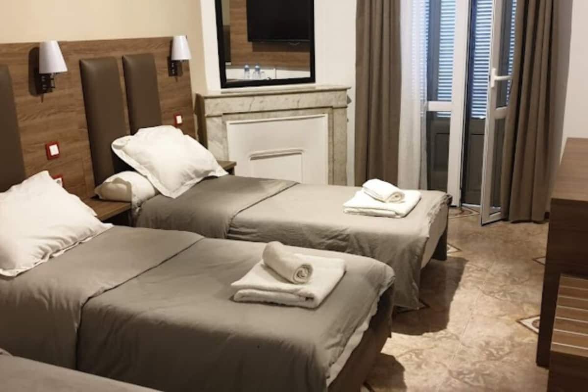 Habitación de hotel con dos camas, un escritorio, un televisor y un baño visible a través de una puerta de vidrio.