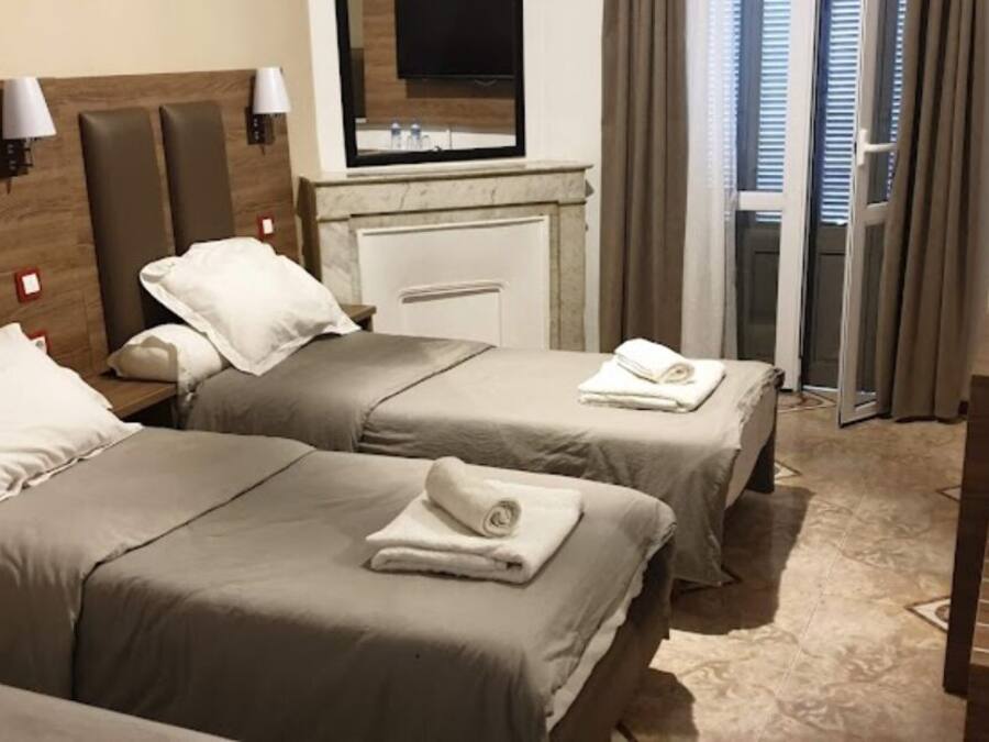 A hotel room with two beds, a desk, a TV, and a bathroom visible through a glass door.