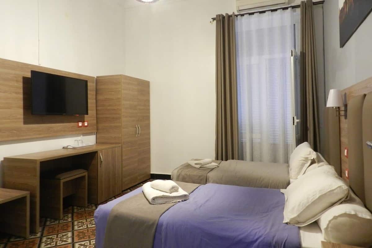 Una habitación de hotel con cama, escritorio, televisor y ventana con cortinas.