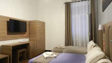 A hotel room with a bed, a desk, a television, and a window with curtains.