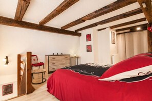 A bedroom with a wooden ceiling, a bed with a red and black bedspread, a wooden dresser, and a chair with a red cushion. - Idéal Séjour Alsace, Gîte de la Liberté ! (Rouffach)