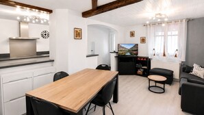 Un salon moderne avec une table à manger en bois, des chaises noires, un canapé noir, un téléviseur et une cheminée.