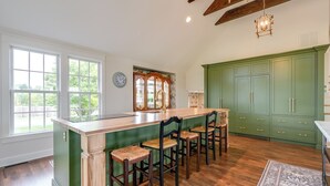 A kitchen with a green island, wooden bar stools, and a large window.