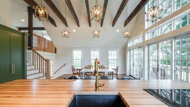 A spacious kitchen with a large island, wooden beams, and large windows.