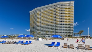 Un hotel frente a la playa con varios balcones, sillas de descanso y sombrillas azules.