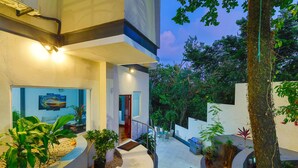 A modern building with a curved staircase leading to a door, surrounded by potted plants and a small outdoor seating area. - Casa Diamante - Top Rated Vacation Home in Manuel Antonio! (Quepos)