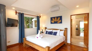 A well-lit bedroom with a wooden bed, a flat-screen TV, and a view of the outdoors through a window. - Casa Diamante - Top Rated Vacation Home in Manuel Antonio! (Quepos)