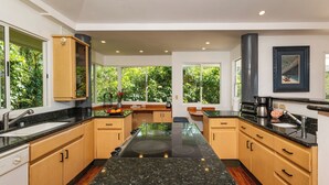 A modern kitchen with a central island, wooden cabinets, and a large window offering a view of greenery. - Casa Diamante - Top Rated Vacation Home in Manuel Antonio! (Quepos)