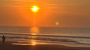Une scène de plage au coucher du soleil, avec des vagues et la silhouette d’une personne qui se promène.
