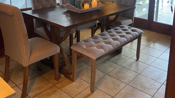 Un espace repas comprenant une table en bois, des chaises rembourrées, un banc et un ventilateur de plafond.