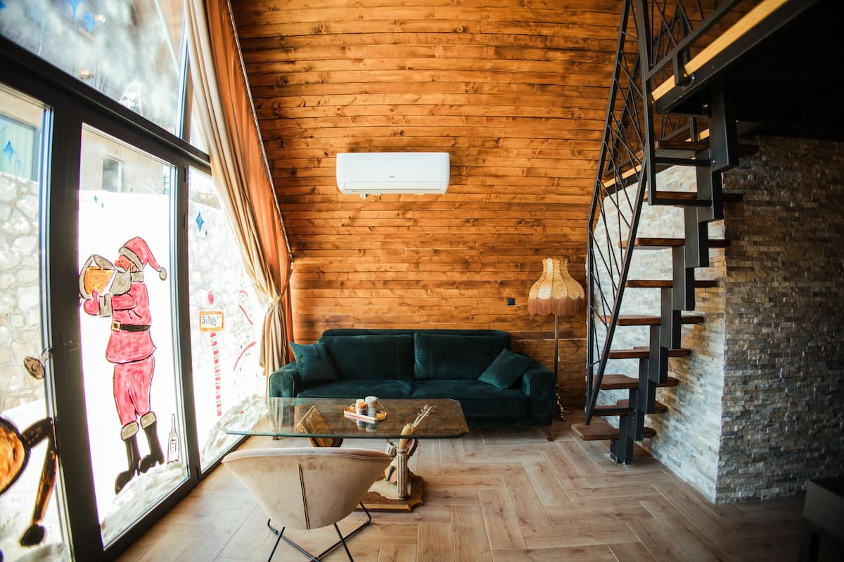 A cozy room with a wooden ceiling, a green sofa, a glass coffee table, and a staircase with a metal railing.