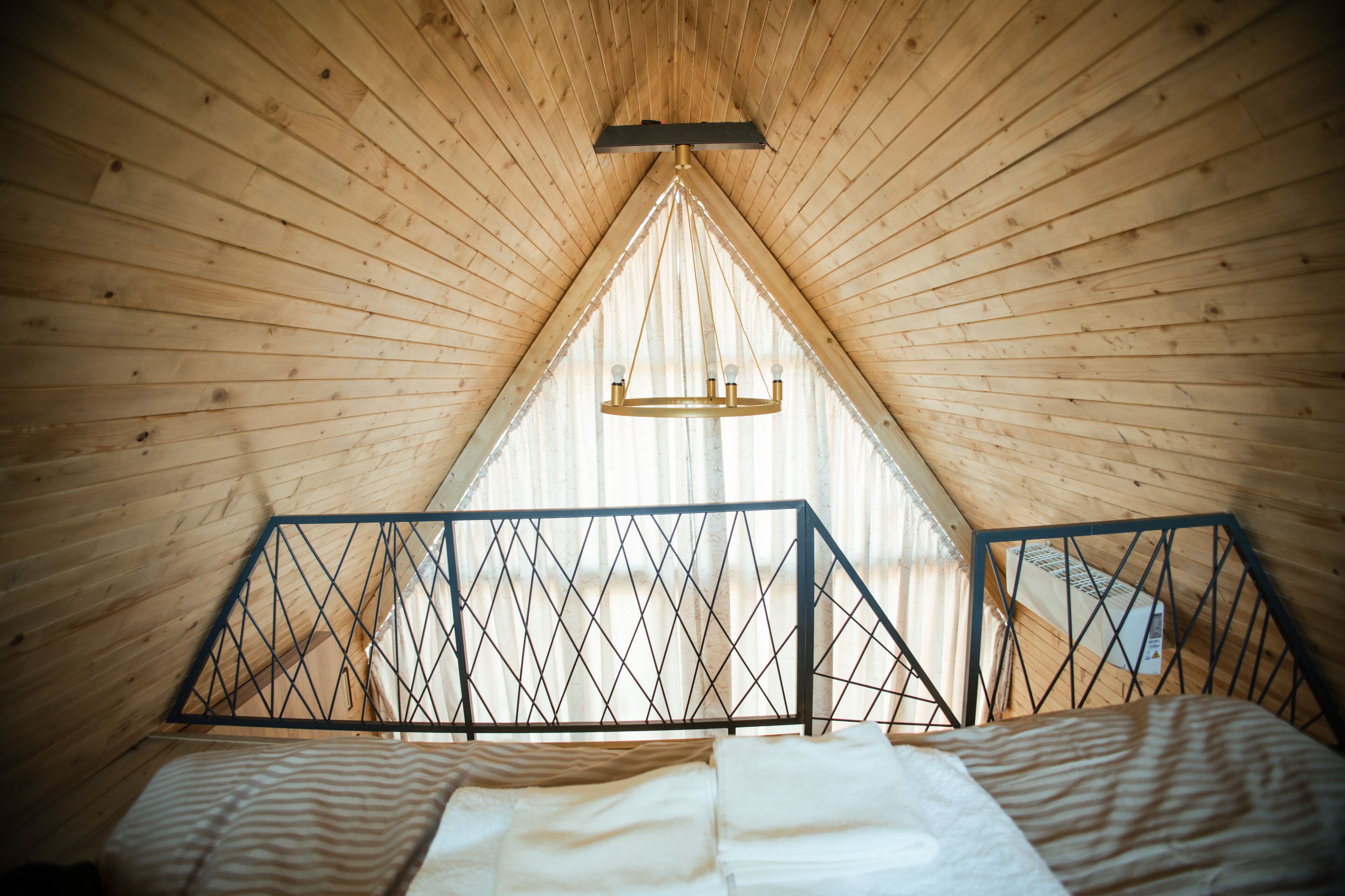 A triangular attic bedroom with wooden walls, a bed with striped bedding, and a chandelier.