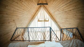 A triangular attic bedroom with wooden walls, a bed with striped bedding, and a chandelier.