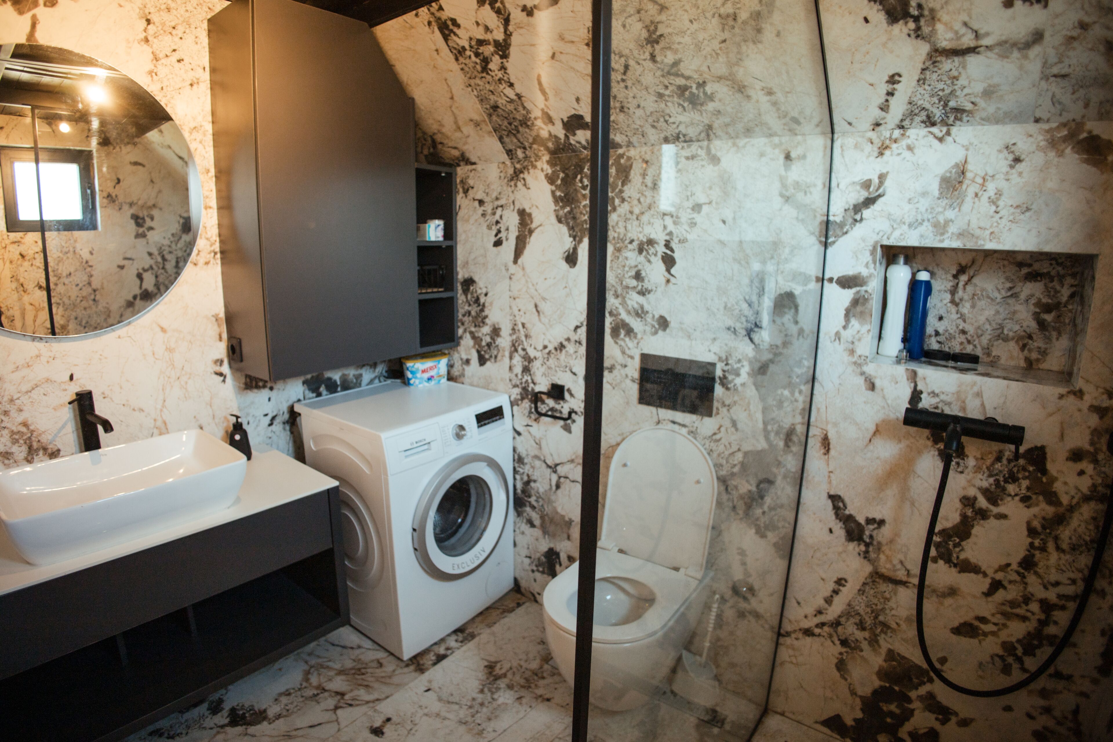 Une petite salle de bain équipée d’un lave-linge, de toilettes, d’un lavabo et d’un miroir.
