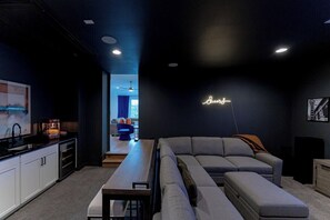 Een moderne woonruimte met een keuken, een grote grijze bank en een neonbord aan de muur.