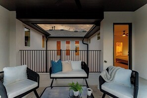 Ein Balkon mit einer Couch, zwei Stühlen, einem Tisch mit Pflanze und Tasse, und Blick auf den Innenraum durch eine Tür.