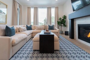 A modern living room with a sectional sofa, a coffee table, a fireplace, and large windows with curtains. - Scenic Hollows Escape with Trails & Outdoor Fun (Jonestown)