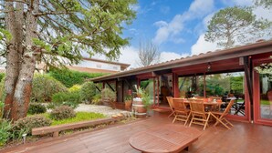 Een terras buiten met houten meubels, een houten bank en een pergola.