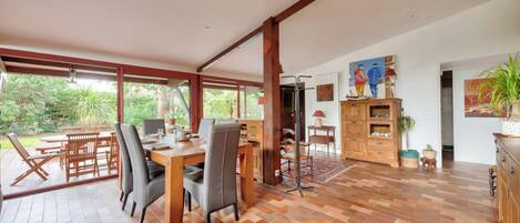 A spacious dining area with a wooden table and chairs, a kitchen area with wooden cabinets, and a view of greenery outside.