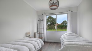 A bedroom with two single beds, a window with curtains, a radiator, a lamp, and a ladder.