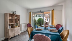 A dining area with a table set for four, a wooden cabinet with shelves, and a view through a glass door.