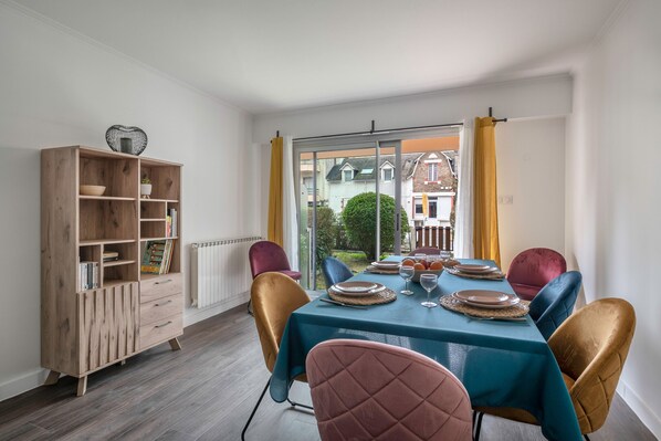 Un comedor con una mesa dispuesta para cuatro, un armario de madera con estantes, y vista a través de un ventanal.