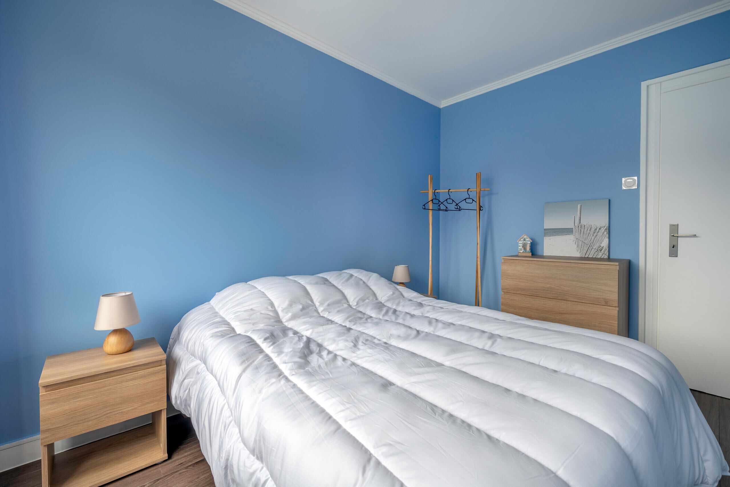 A bedroom with a bed, nightstands, a lamp, a coat rack, and a dresser.