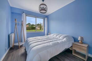 Un dormitorio con una cama grande, una ventana que da a zonas verdes, una escalera de madera y una mesita de noche con lámpara.