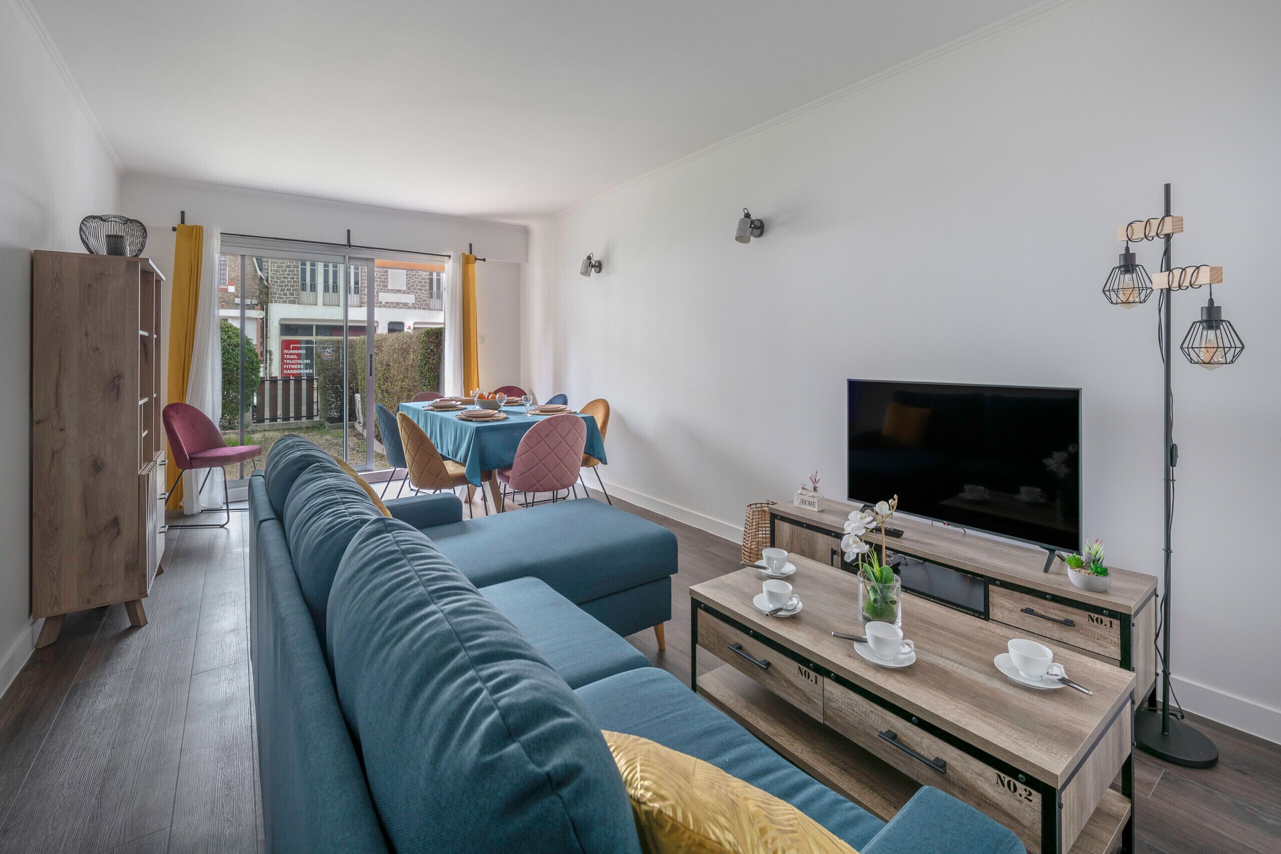 Ett modernt vardagsrum med en soffa, ett soffbord, en tv och en matplats med stolar och ett bord.