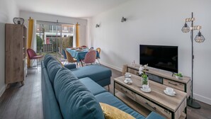 A modern living room with a sofa, a coffee table, a TV, and a dining area with chairs and a table.