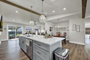 A spacious kitchen with a large island, pendant lights, and a view to the outdoors. - Crystal Cow Haus Luxury Home-Pool-HotTub-Near Main (Fredericksburg)