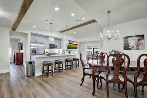 A spacious kitchen with modern appliances, a dining area with wooden chairs, and a chandelier. - Crystal Cow Haus Luxury Home-Pool-HotTub-Near Main (Fredericksburg)