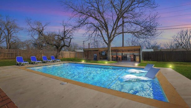 A rectangular swimming pool with a wooden deck, surrounded by blue lounge chairs.